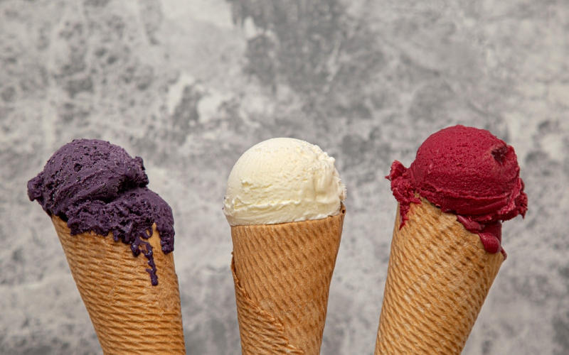 helados con cucurucho de varios sabores (mora, vainilla, frambuesa) sobre fondo gris